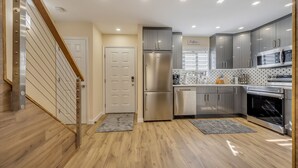 A modern kitchen with stainless steel appliances, wooden flooring, and a staircase leading to another level. - Ski on/off home in Camelback (Tannersville)