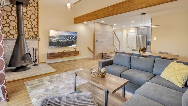 A modern living room with a fireplace, a grey sofa, a wooden coffee table, and a dining area in the background. - Ski on/off home in Camelback (Tannersville)