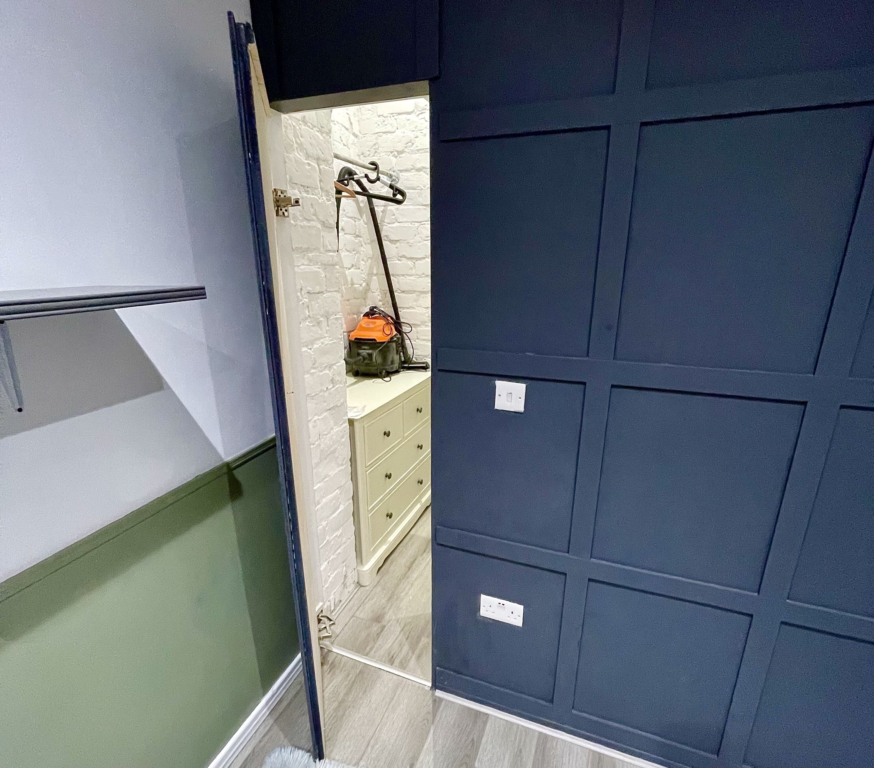 Ein Zimmer mit weißer Ziegelwand, einer blauen Tür und einem kleinen, weißen Schrank mit Schubladen.