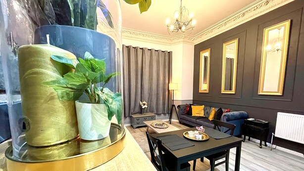 Una sala moderna con comedor, que incluye una lámpara de araña, un sofá con cojines y una planta en maceta.