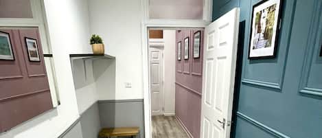 A hallway with a bench, a plant, and a door leading to another room.