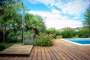A wooden deck with a pool, surrounded by lush greenery and a clear sky. - Villa Grey (Kastela)