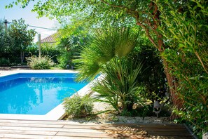 A swimming pool surrounded by lush greenery and a wooden deck. - Villa Grey (Kastela)