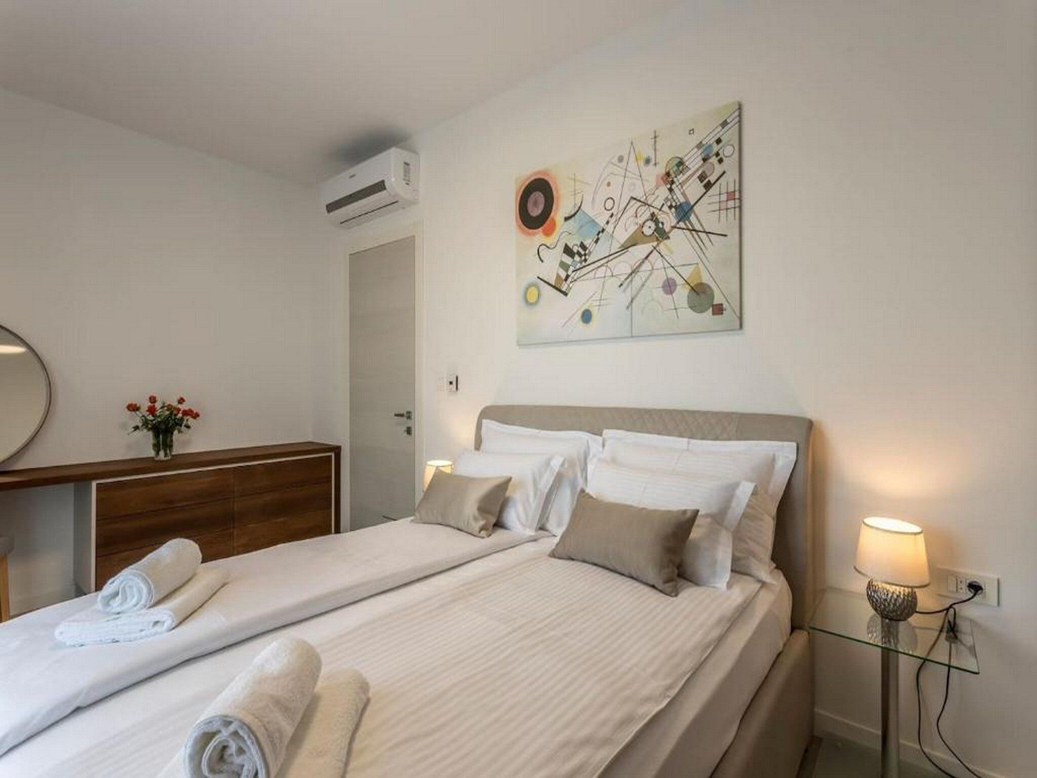 Una habitación de hotel con dos camas, una mesita de noche con lámpara, aire acondicionado instalado en la pared y un cuadro.