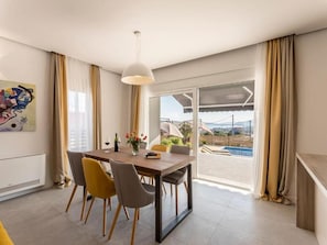 A modern dining area with a table, chairs, and a view of a pool and landscape. - Villa Grey (Kastela)