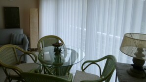 Een woonkamer met een glazen tafel, omringd door rieten stoelen, een bank en een lamp.
