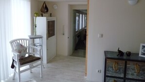 Een woonkamer met een witte stoel, een bijzettafeltje en een kastje met decoratieve objecten.