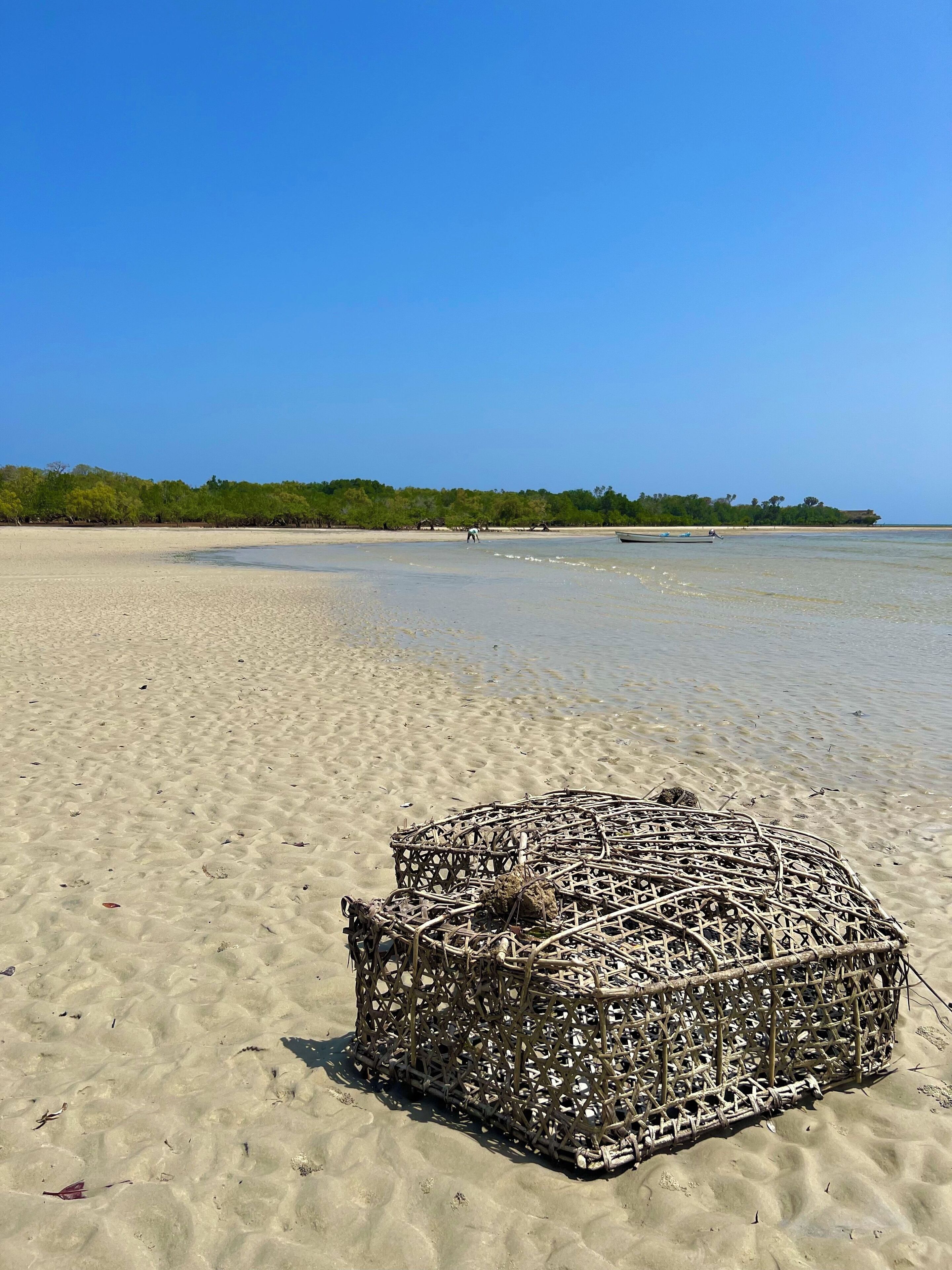 A beach with a large woven basket in the sand.