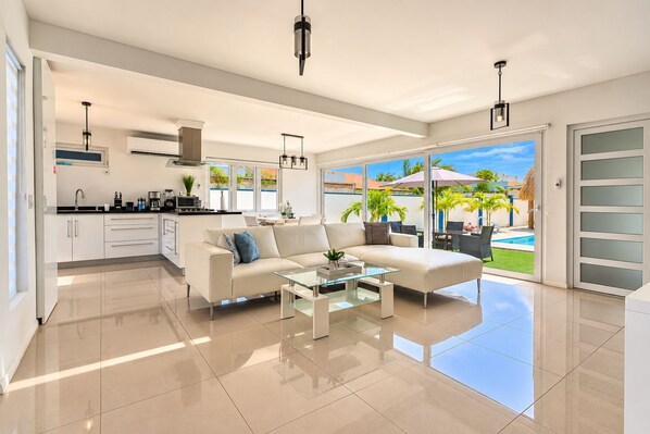 A modern living room with a sofa, coffee table, and a view of a swimming pool. - New-Modern Villa Island Escape, 10 Minute Drive to Beaches (Oranjestad)