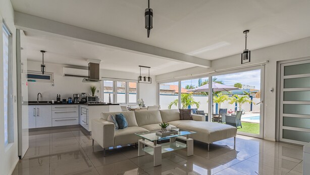 A modern living room with a sofa, coffee table, and a view of the outdoor pool area. - New-Modern Villa Island Escape, 10 Minute Drive to Beaches (Oranjestad)