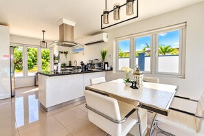 A modern kitchen with a central island, white cabinetry, and a dining area with a white table and chairs. - New-Modern Villa Island Escape, 10 Minute Drive to Beaches (Oranjestad)