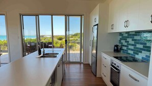 Una cocina moderna con una isla grande, un refrigerador y vista al océano a través de amplias ventanas.