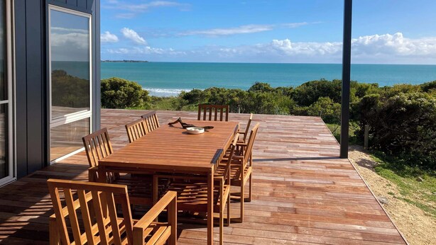Una terraza de madera con una mesa y sillas, con vistas a la costa.
