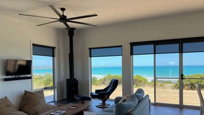 Una sala de estar moderna con un ventanal grande, un ventilador de techo, chimenea, sofá y televisor.