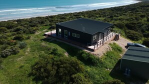 Una casa moderna con techo plano, ventanas amplias y una terraza con vista a la playa.