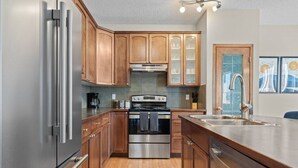 A modern kitchen with wooden cabinets, stainless steel appliances, and a large island with a sink. - Blue Moon | Playground | Backyard | Pet Friendly (Calgary)