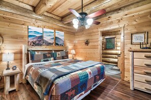 Ein Schlafzimmer in einer Blockhütte mit einem Bett, einem Deckenventilator und einem Fenster.
