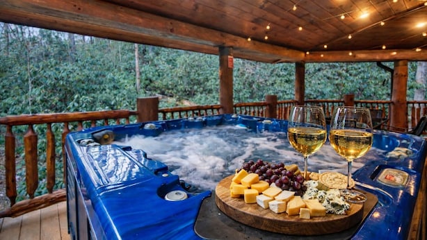 Een hottub met een houten terras, omgeven door groen.