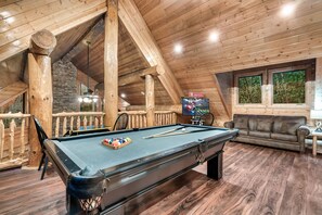 A wooden interior with a pool table, a sofa, and a TV.