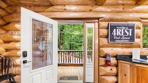 Een houten cabin interieur met een glazen deur naar een terras, een bordje met 4REST Creek Retreat en een brandblusser.