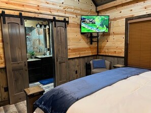 A bedroom with a bed, a TV mounted on the wall, a sliding door, and a small table.