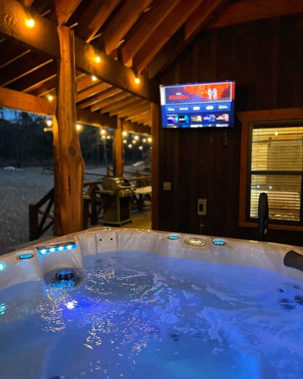 A hot tub with blue LED lights, a wooden deck, and a television mounted on the wall.