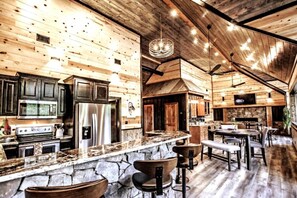 A rustic kitchen with stone countertops, wooden cabinets, and a stone fireplace.