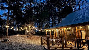 A rustic wooden building with a covered outdoor seating area and string lights. - Cozy Cabin W/ 2 King Suites, Pet Friendly, Hot tub (Broken Bow)