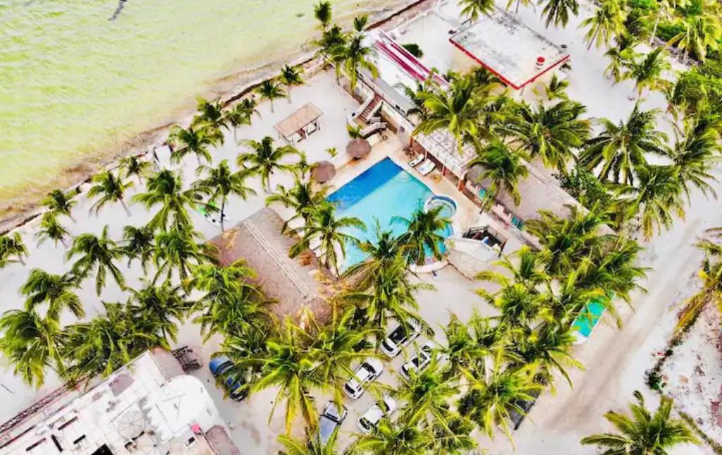 Oversigtsbillede af et resort med en swimmingpool omgivet af palmer, en strand og nogle bygninger.