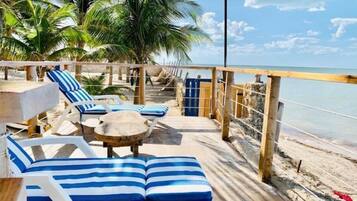 Une terrasse au bord de la plage, dotée de chaises longues et d’une table, avec vue sur l’océan.