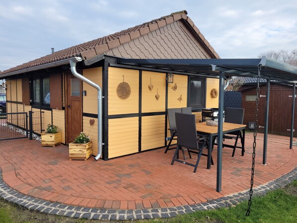 A house with a patio area featuring a table and chairs, a covered seating area, and a brick pathway.