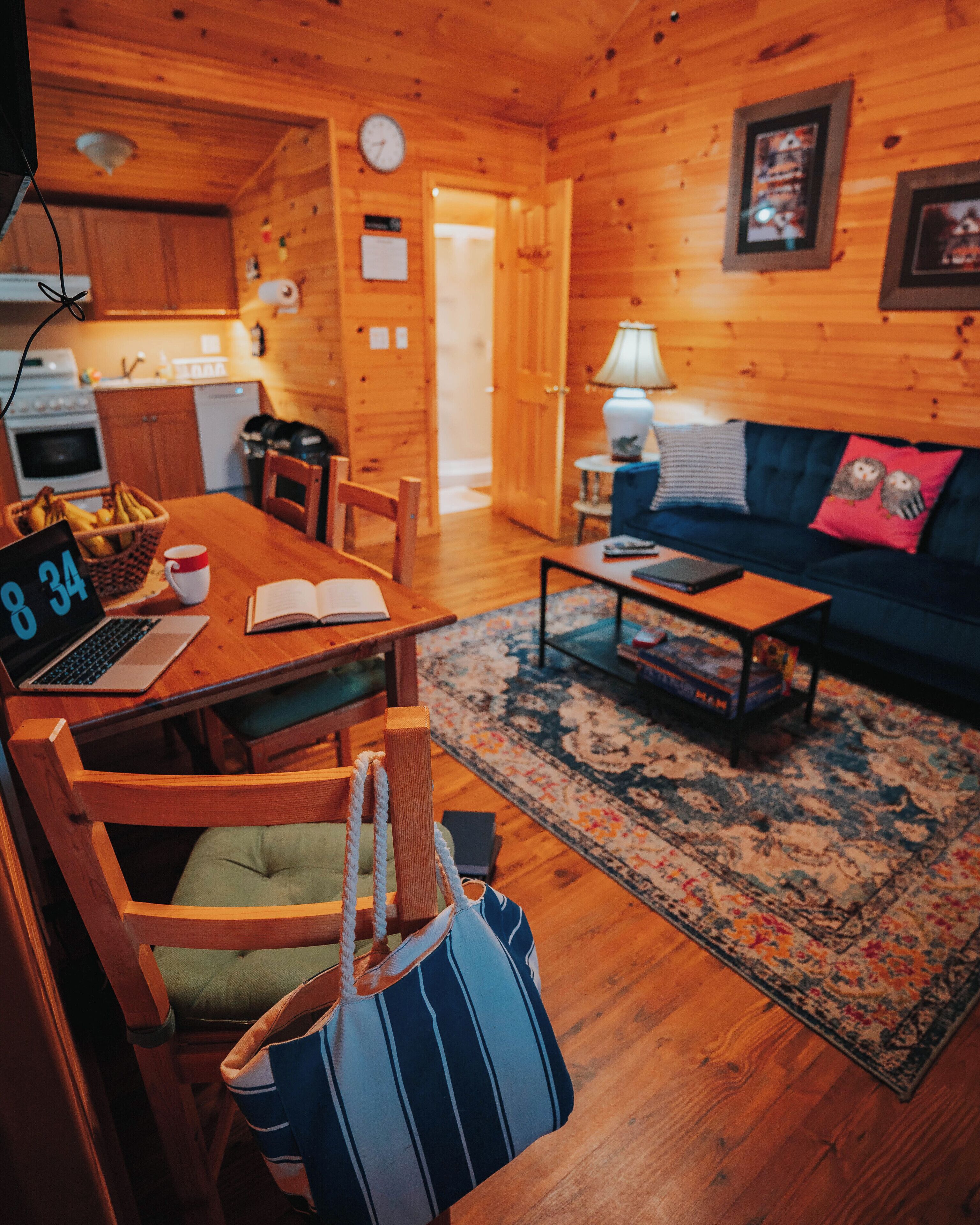 A cozy wooden cabin interior with a dining table, chairs, a sofa, a coffee table, and a kitchen area.