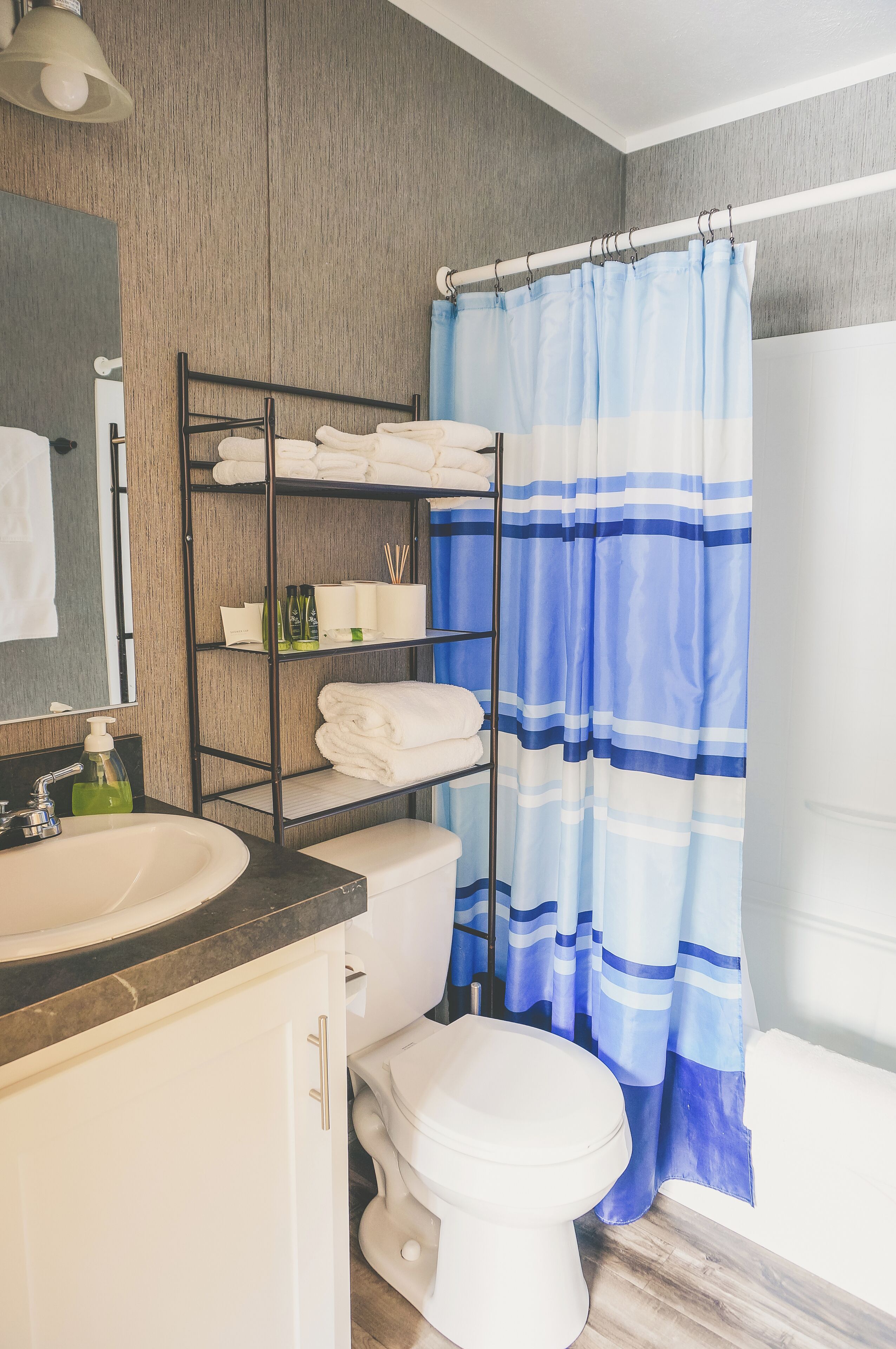 A bathroom with a wooden vanity, a white sink, a toilet, and a shower curtain with blue stripes.