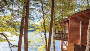 A wooden cabin with a balcony overlooking a lake surrounded by trees. - Motel Long Lake and Cottages (Long Lake)