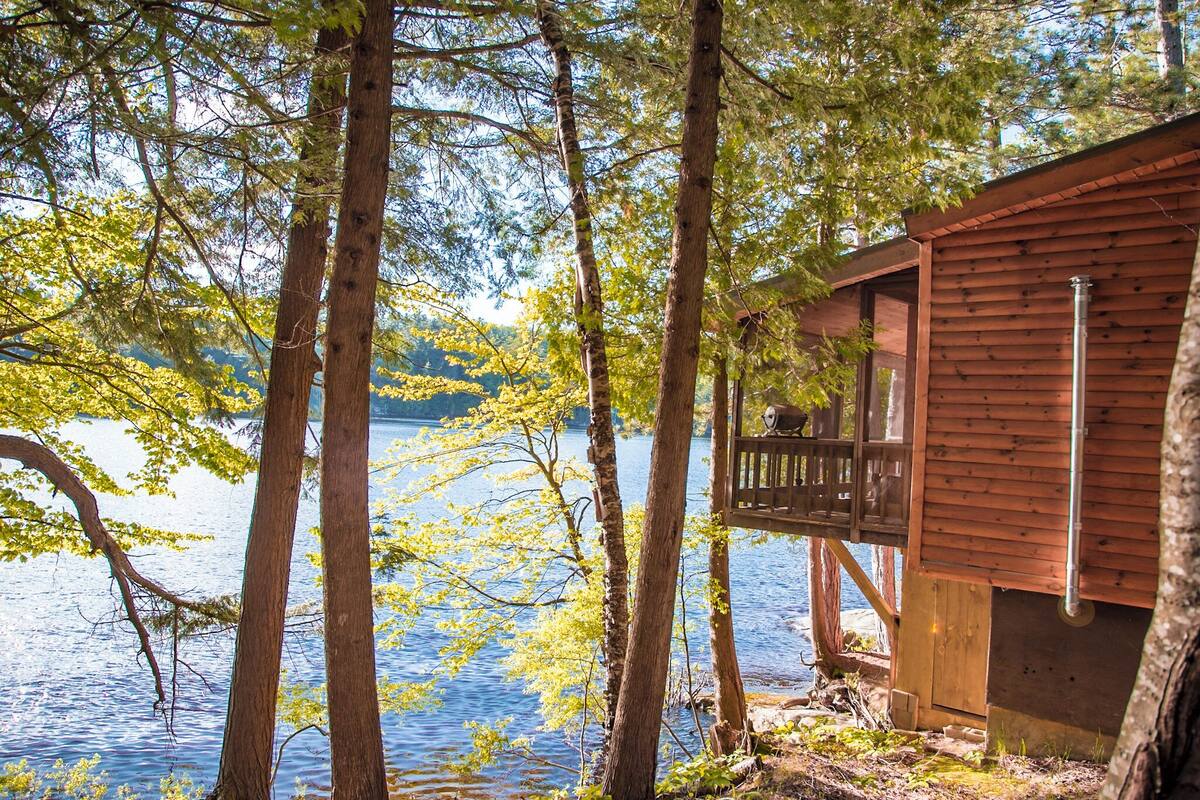 A wooden cabin with a balcony overlooking a lake surrounded by trees.