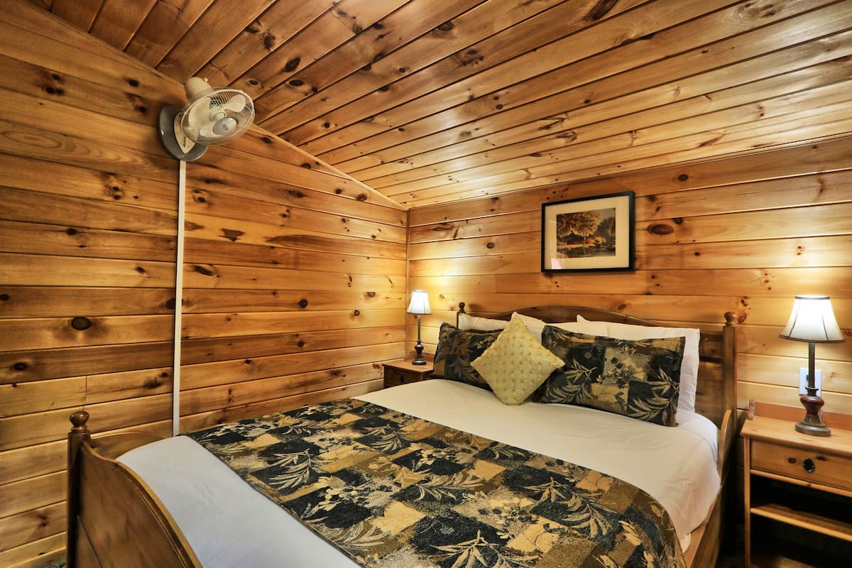 A wooden-paneled room with a bed, two bedside lamps, and a ceiling fan.