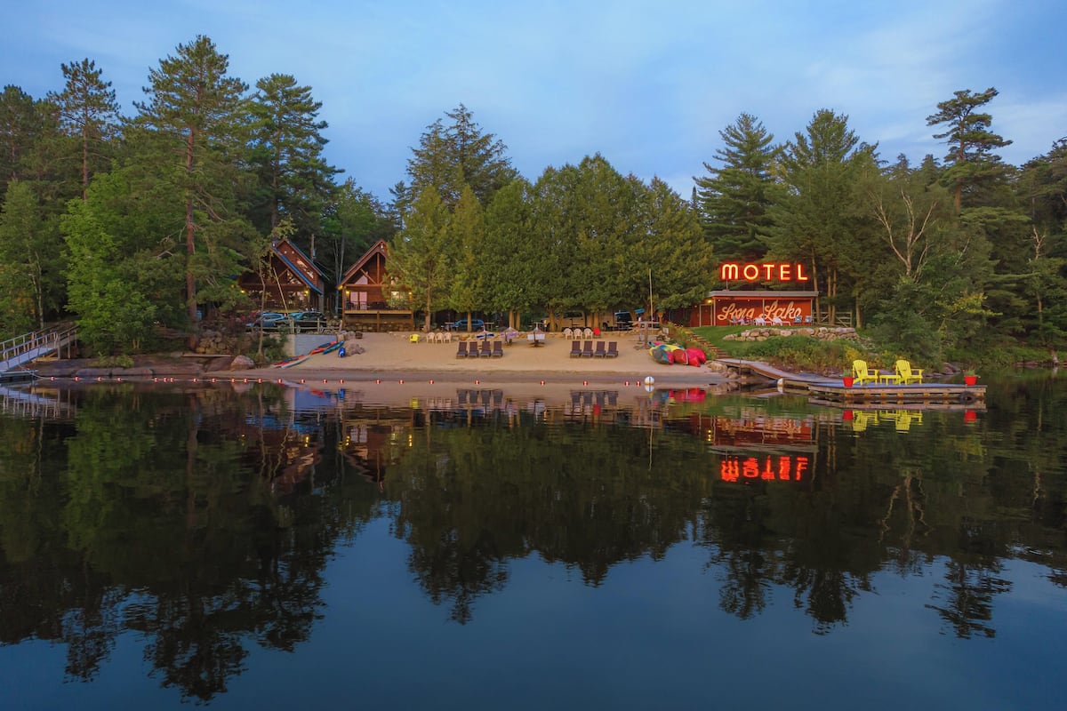 A lakeside motel with a reflection in the water, surrounded by trees.