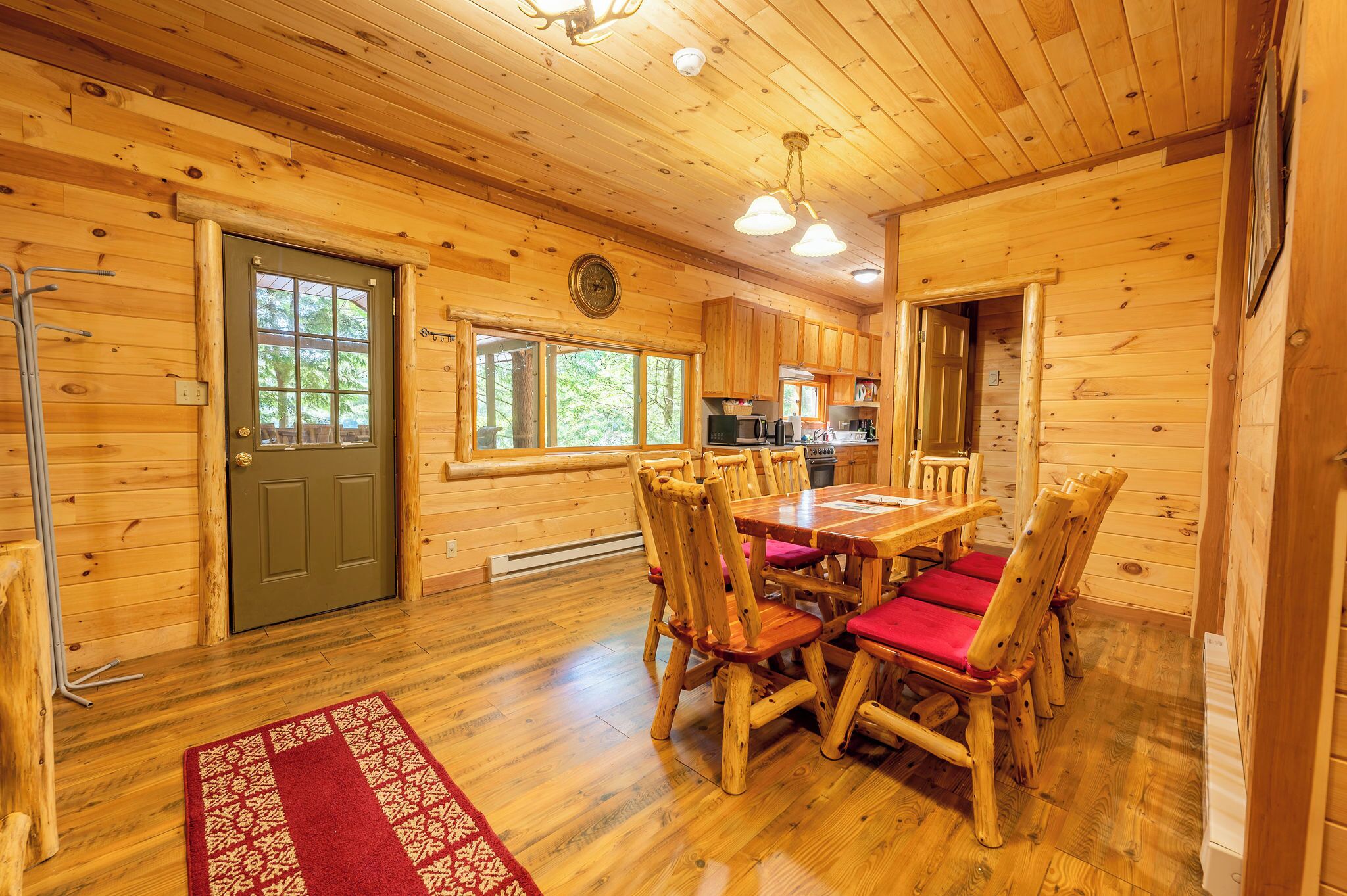 Interior de una cabaña de madera con una mesa de comedor, sillas, una zona de cocina y una puerta con ventana.