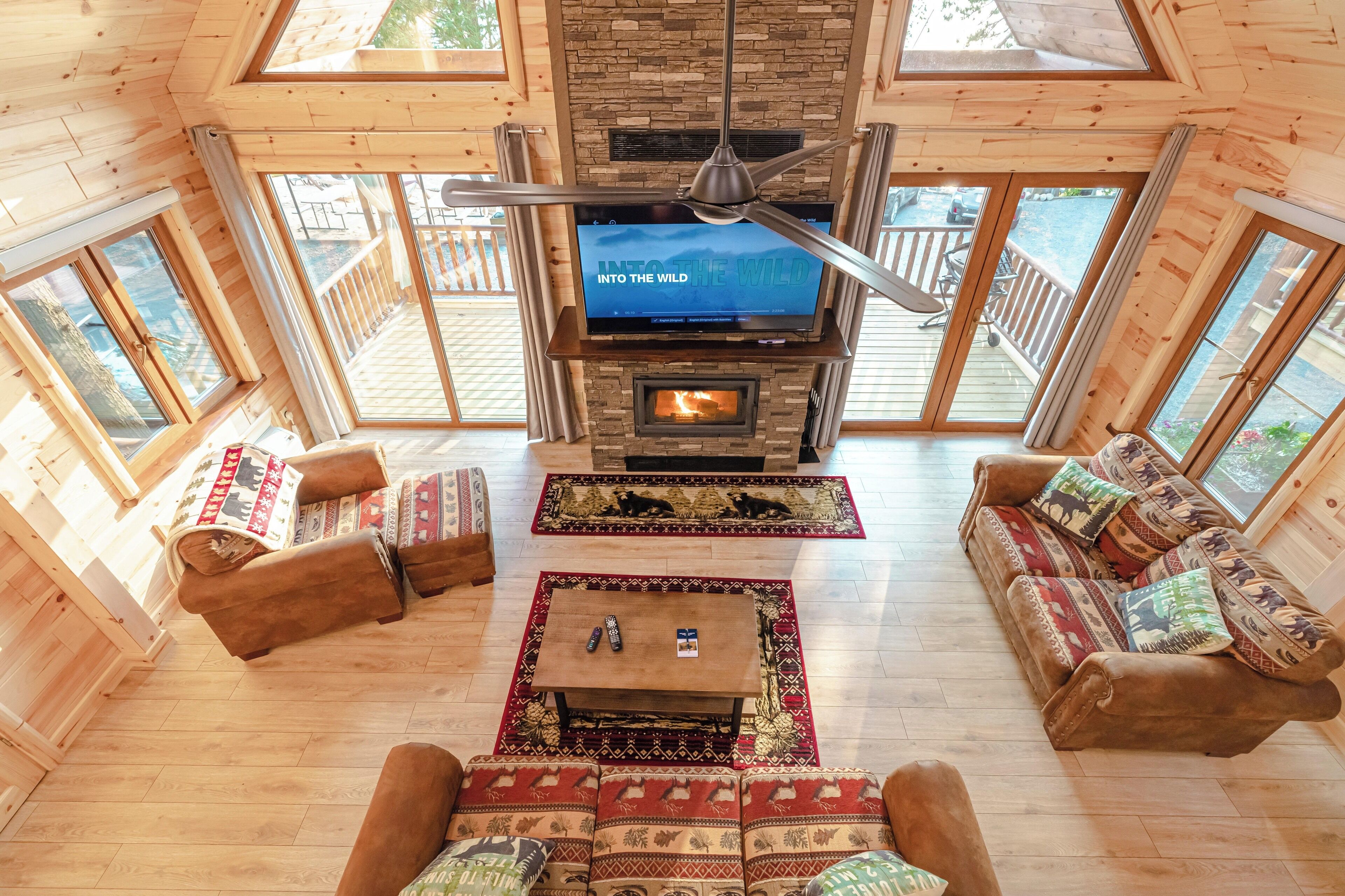 A cozy cabin interior with a fireplace, wooden furniture, and large windows.
