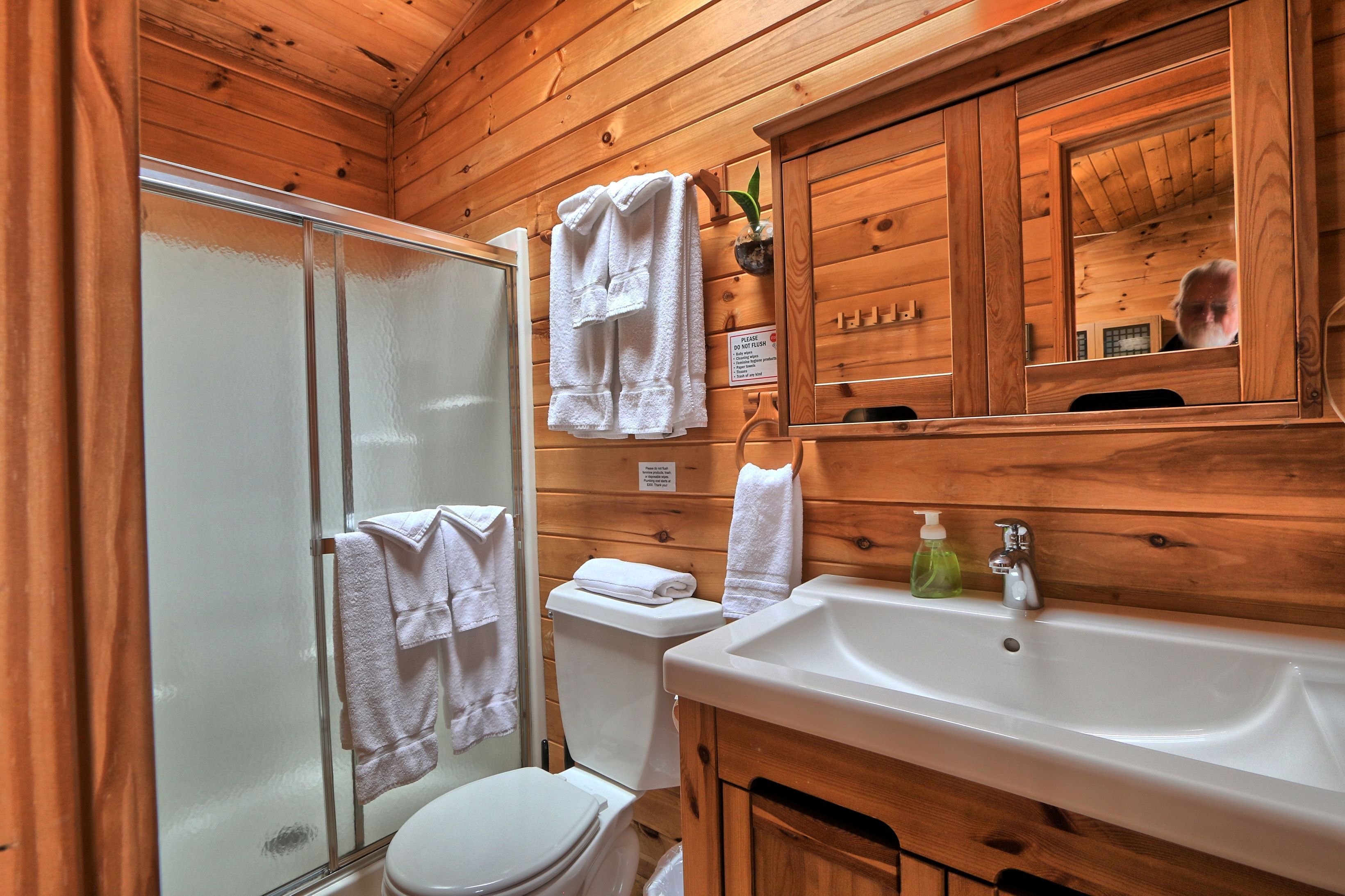 A wooden cabin bathroom with a shower, toilet, sink, and a mirror.