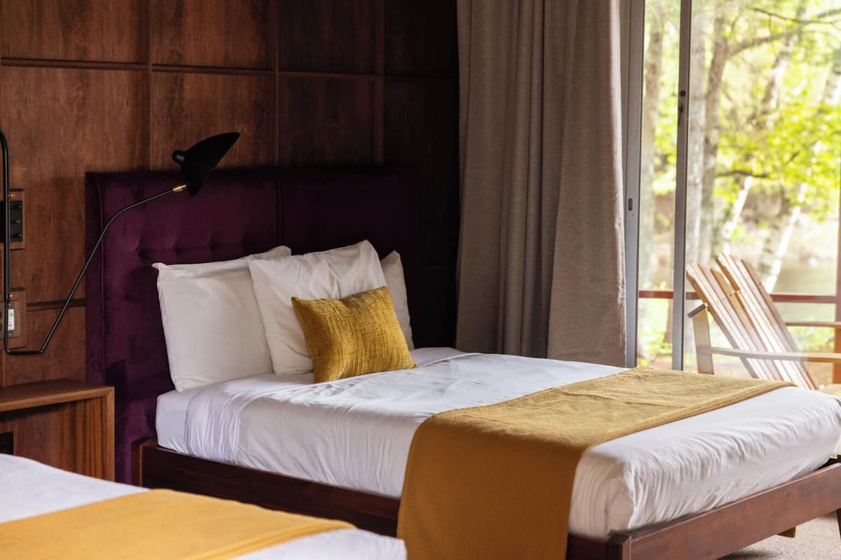 A bed with white linens, a gold throw blanket, and a purple headboard.