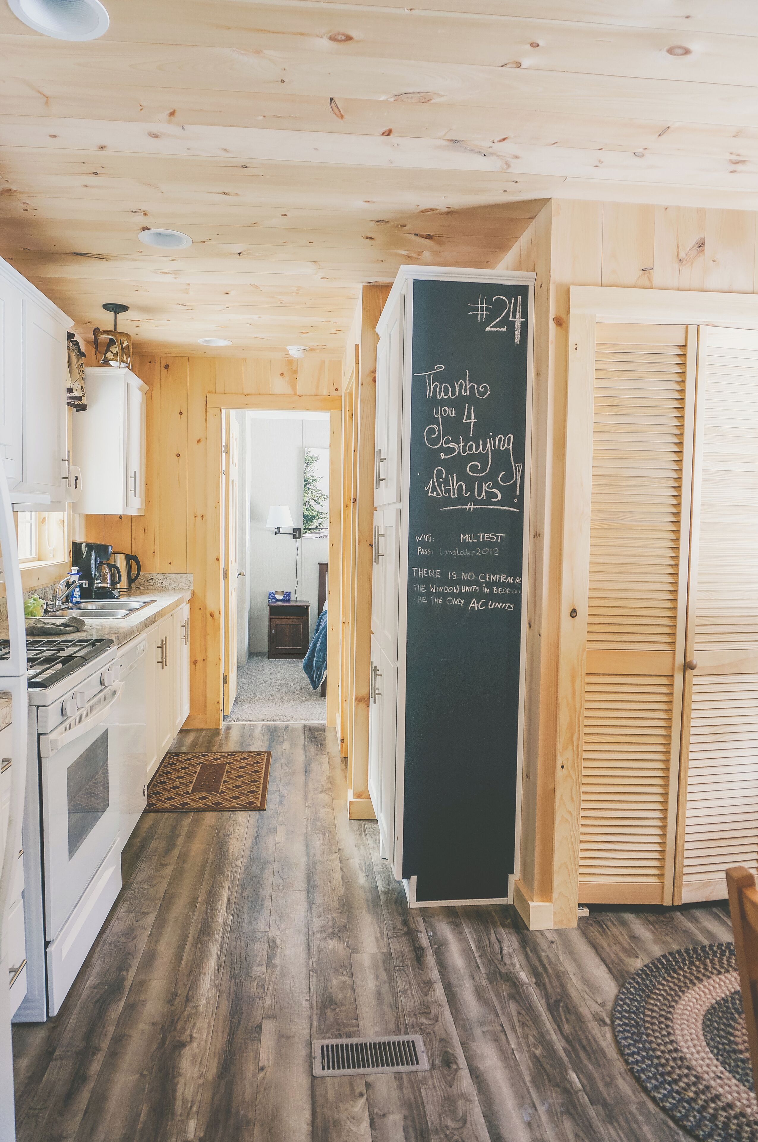 A wooden interior with a kitchen, a chalkboard with a message, and a wooden floor.