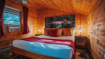 Une chambre rustique en bois, avec un lit, un ventilateur de plafond, une fenêtre avec des rideaux et un tableau accroché au mur.