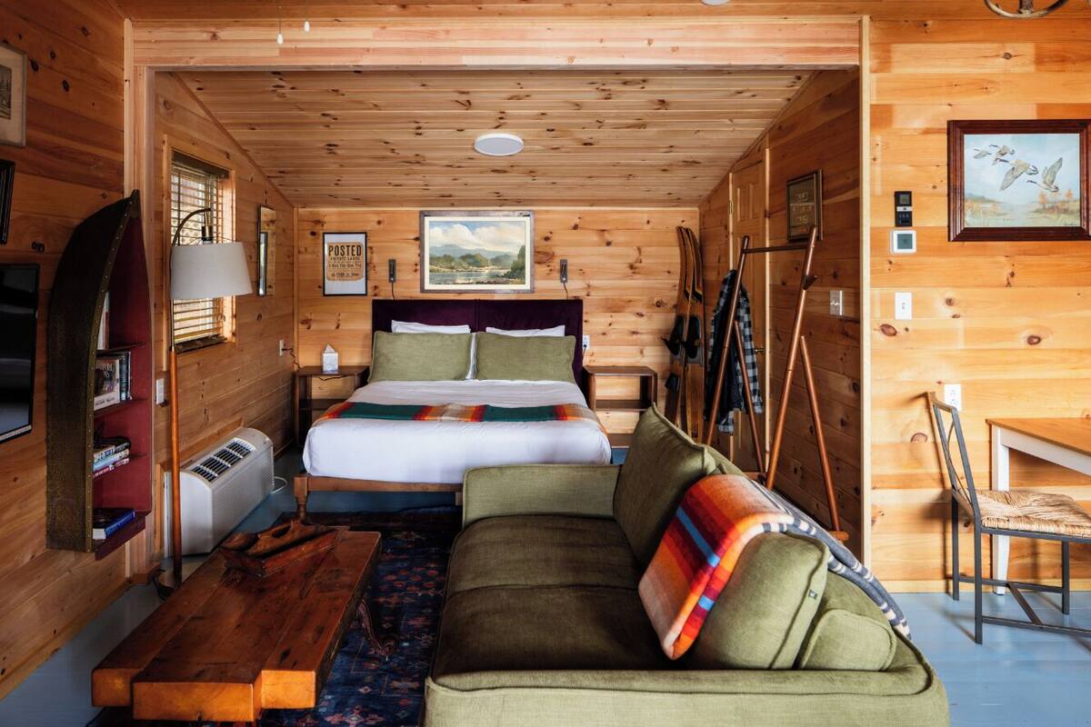 A cozy cabin interior with a bed, sofa, and wooden walls.