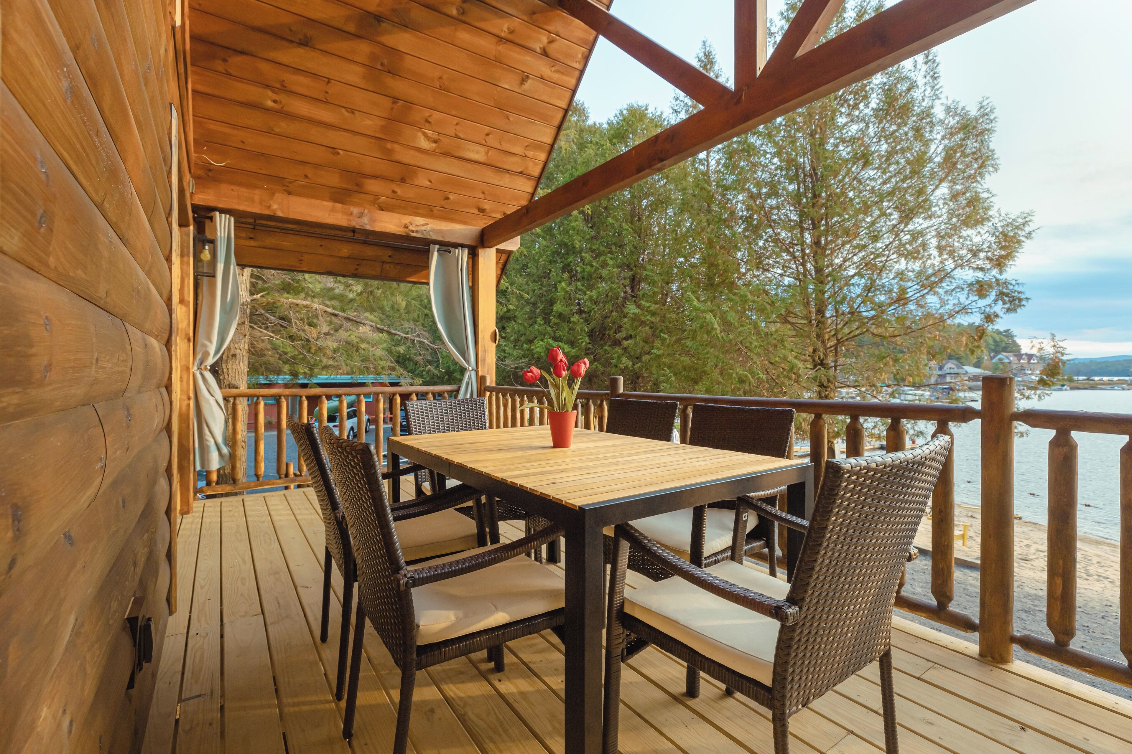 A wooden deck with a table and chairs, overlooking a body of water and trees.