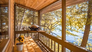 A wooden deck with a table and a grill, overlooking a snowy landscape. - Motel Long Lake and Cottages (Long Lake)