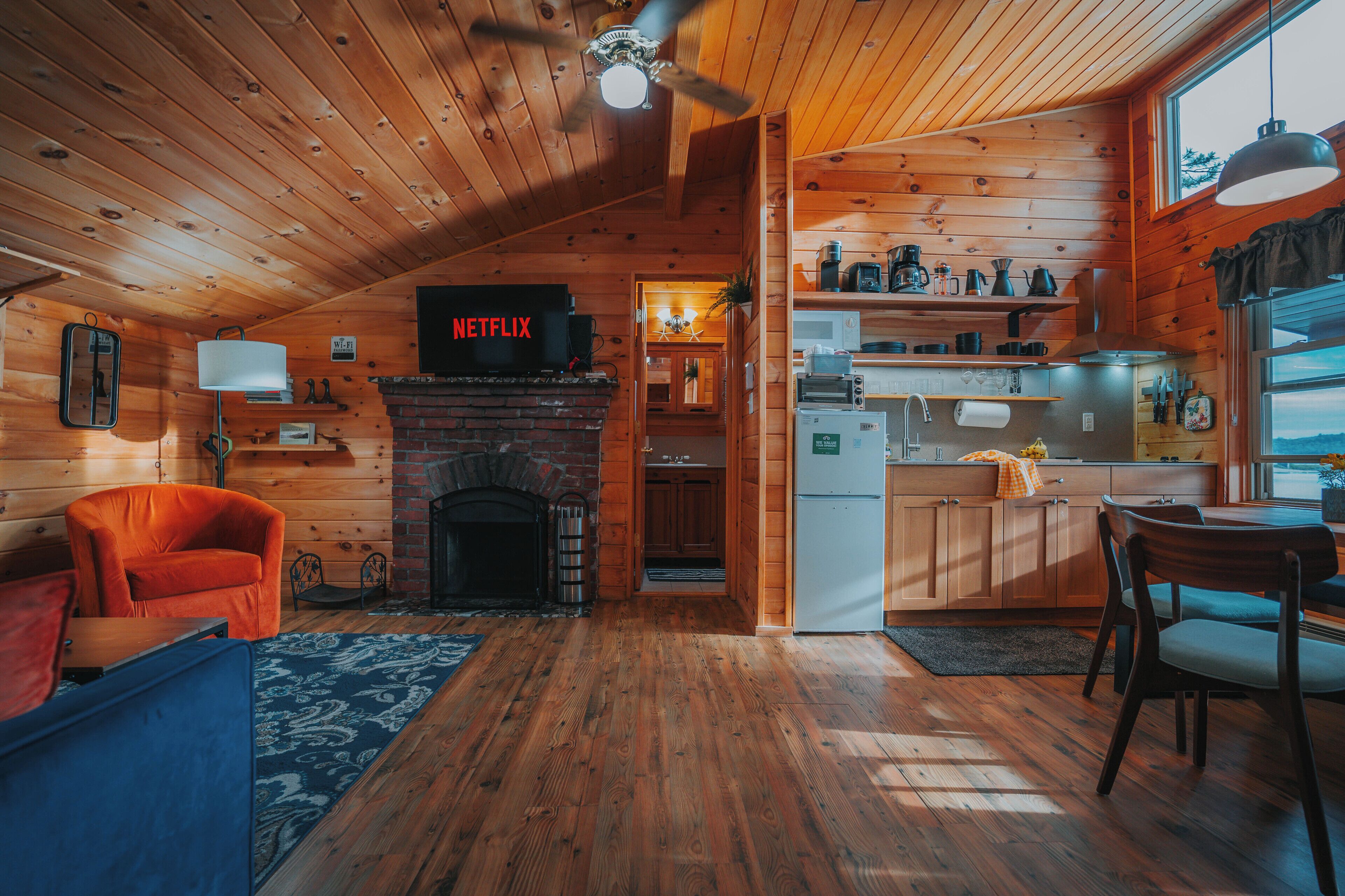 A cozy cabin interior with a fireplace, wooden walls, a kitchen area, and a Netflix sign.