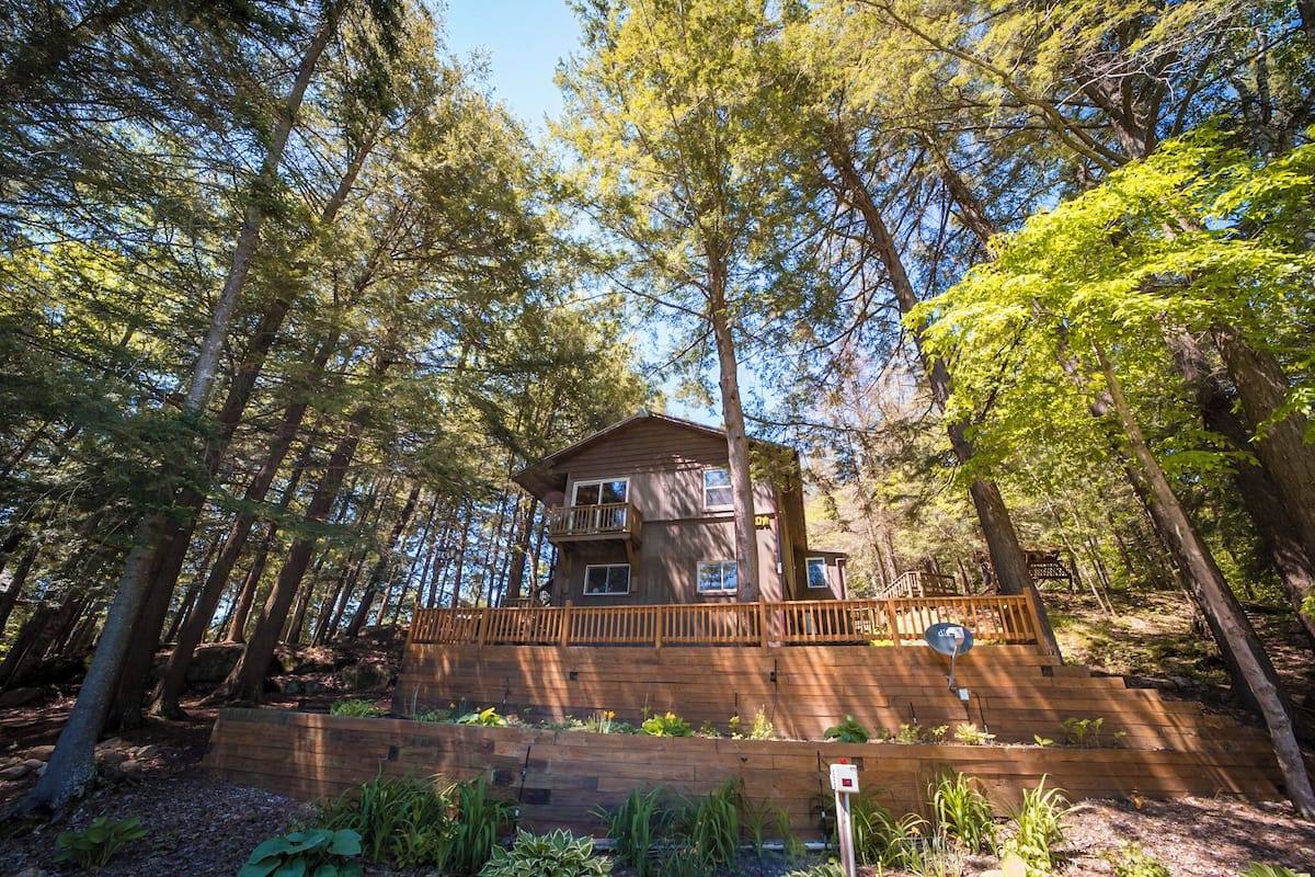 A cabin surrounded by tall trees, with a wooden deck and a satellite dish.