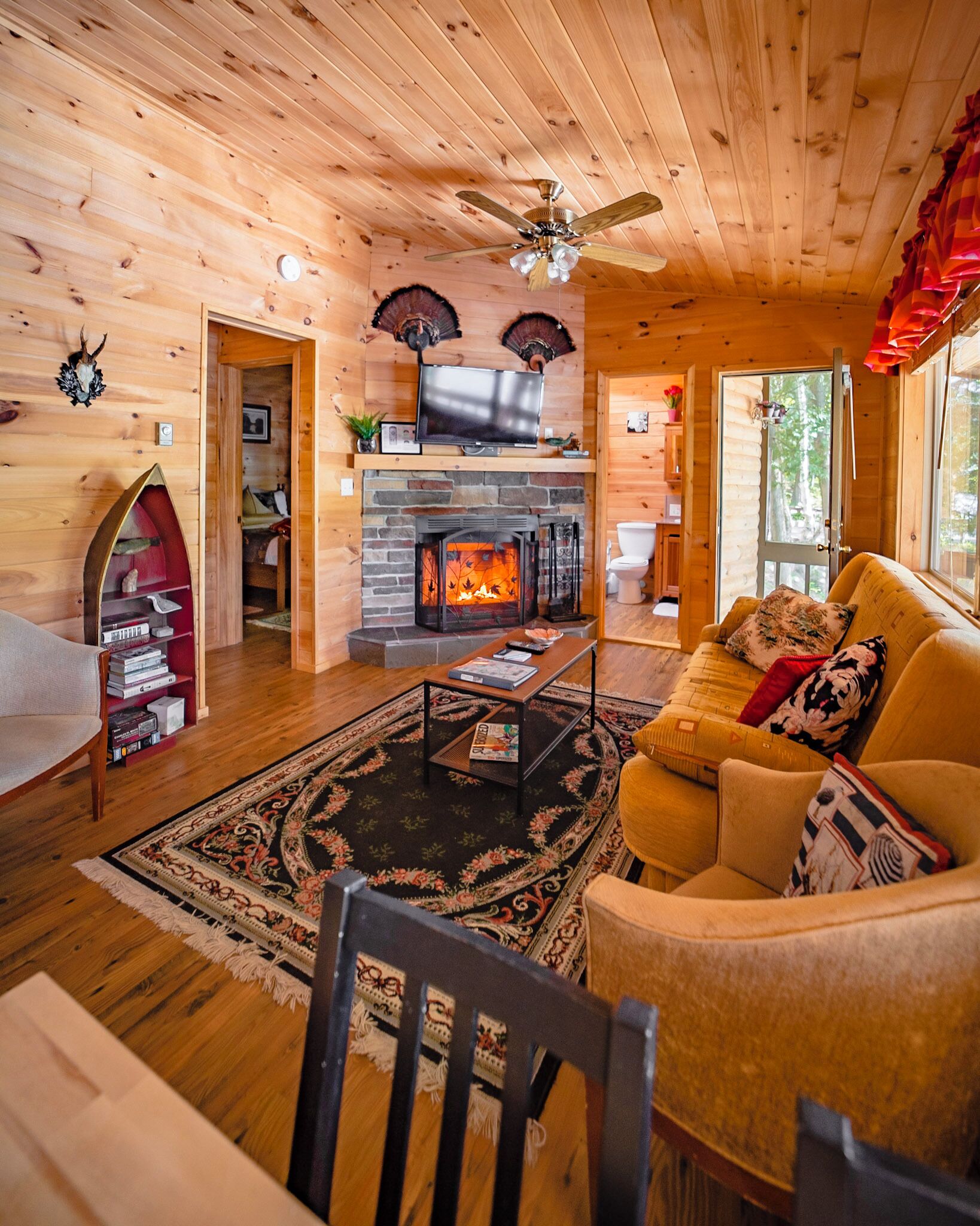 A cozy cabin interior with a fireplace, wooden walls, a sofa, and a television.