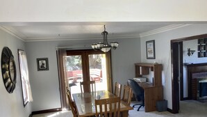 Zona pranzo con tavolo e sedie in legno, un lampadario e vista sull'esterno.